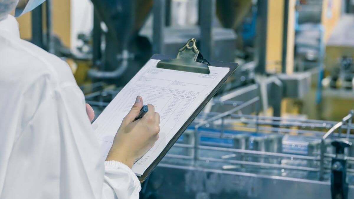 A person reviewing quality control form on clipboard in a modern factory.